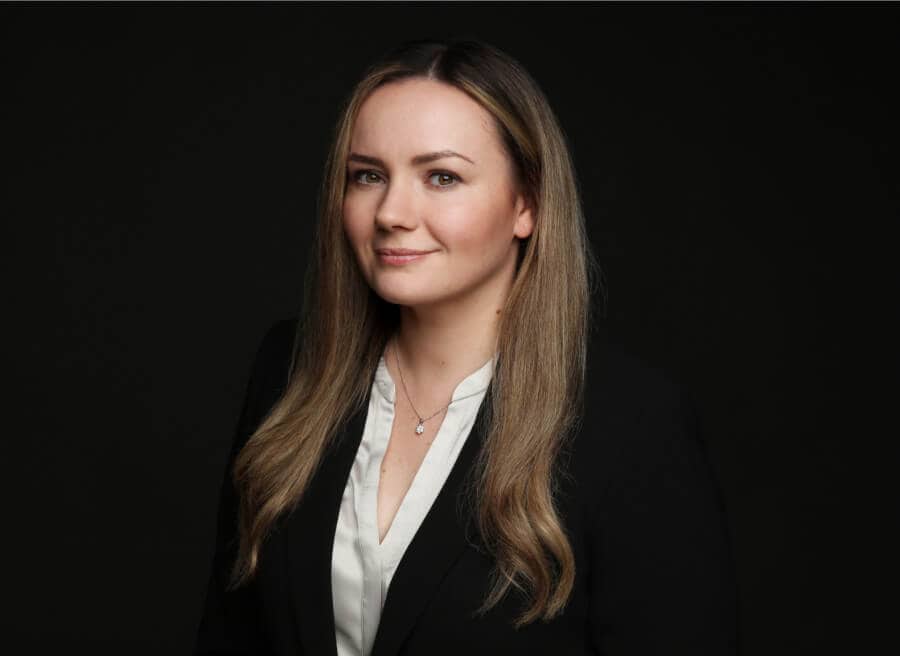 A photo of Elena Barbier with long brown hair smiling softly, wearing a white blouse and black blazer.