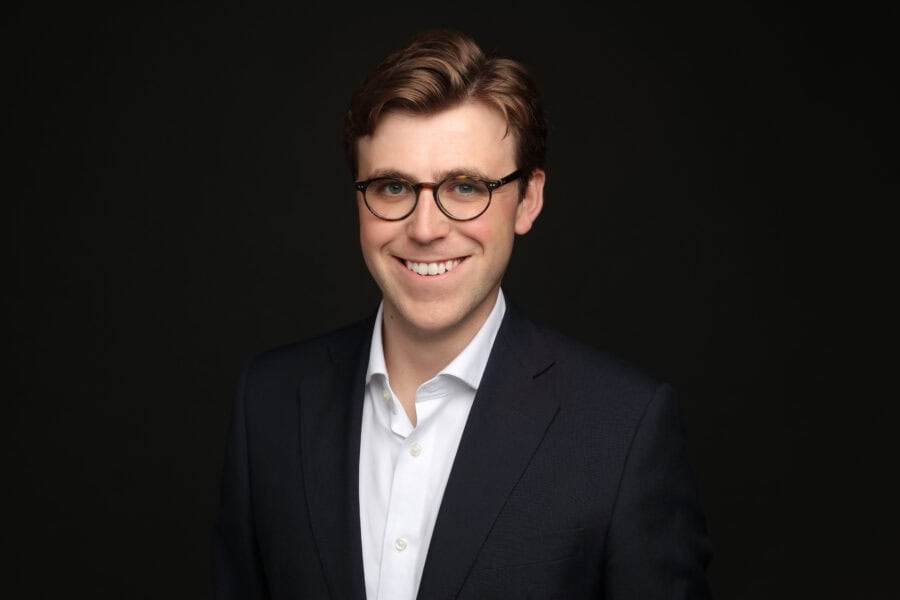 An image of Hugo Andrews in a dark suit and white shirt against a dark background.