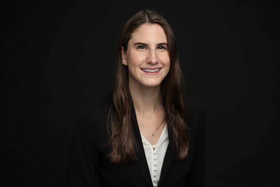Kendyl Spearing with long brown hair against a plain black background, wearing a black blazer and a white blouse.
