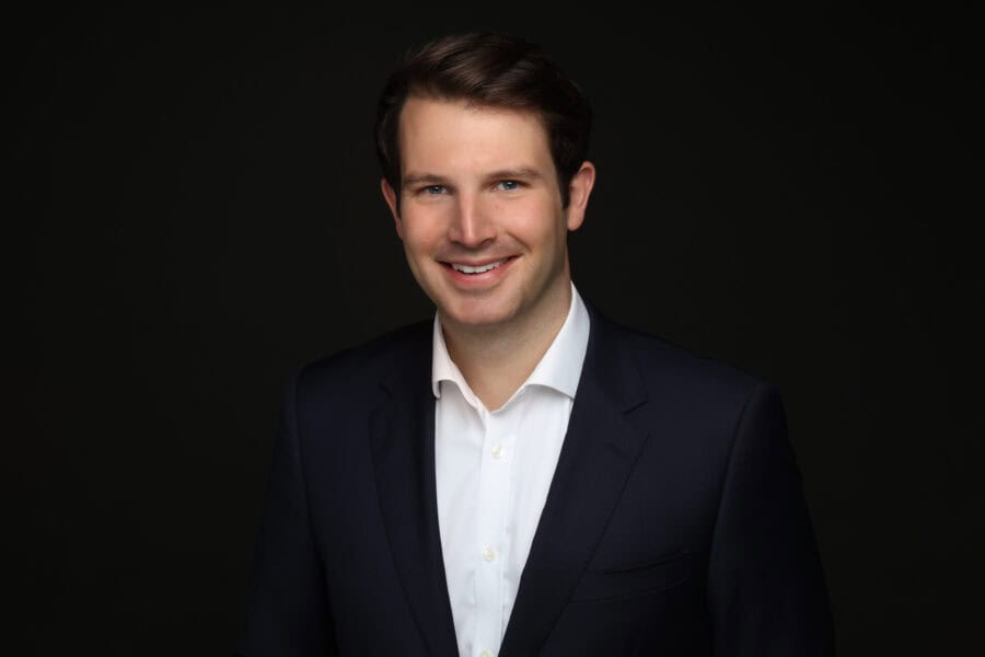 Chris Bentley in a navy blue suit against a dark background conveying professionalism.