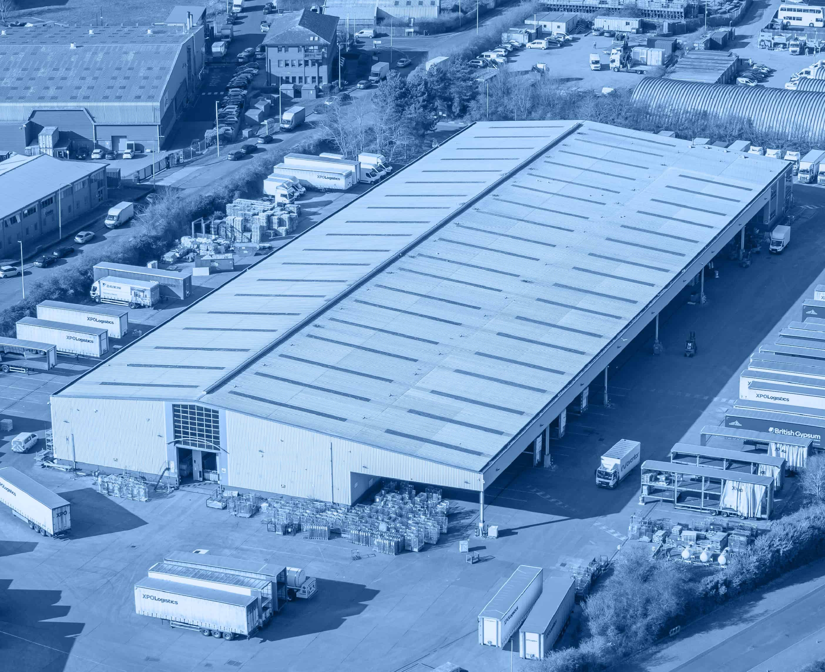 Aerial view of a large industrial warehouse surrounded by trucks and shipping containers. The setting conveys a busy and organised logistic center.