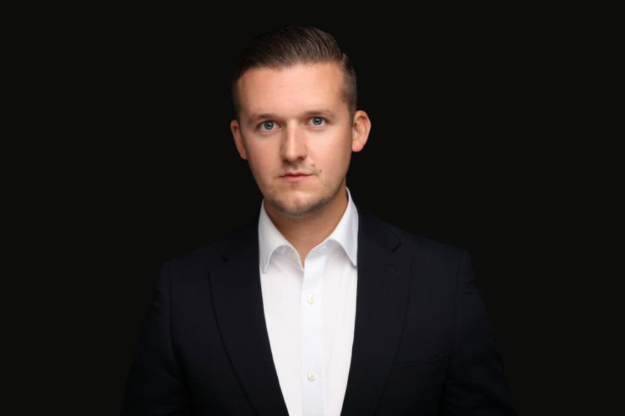 A photo of Dan Gray in a dark suit jacket against a black background. The tone is professional and serious.