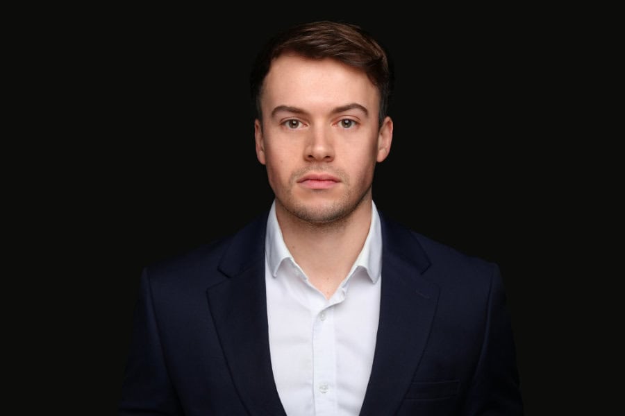 A photo of Max Pearson in a navy suit, staring confidently at the camera.