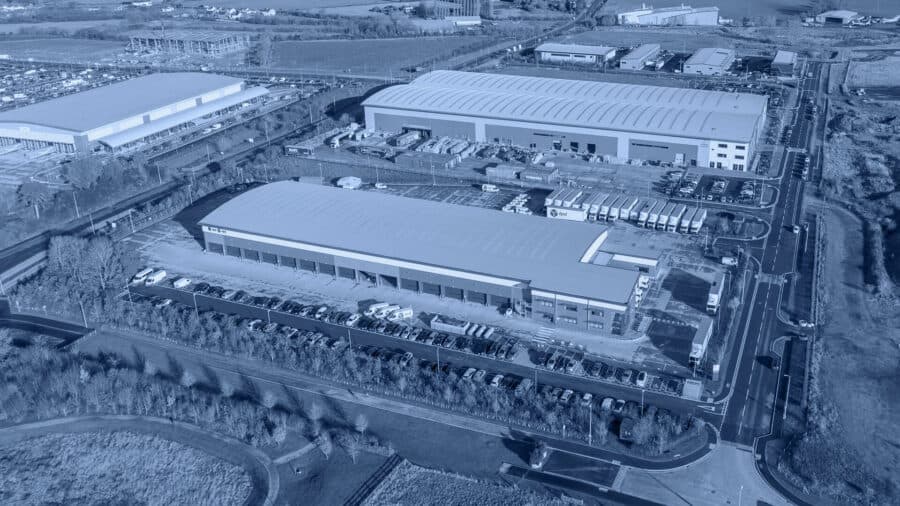 Aerial view of an industrial complex with large warehouses surrounded by roads and fields.