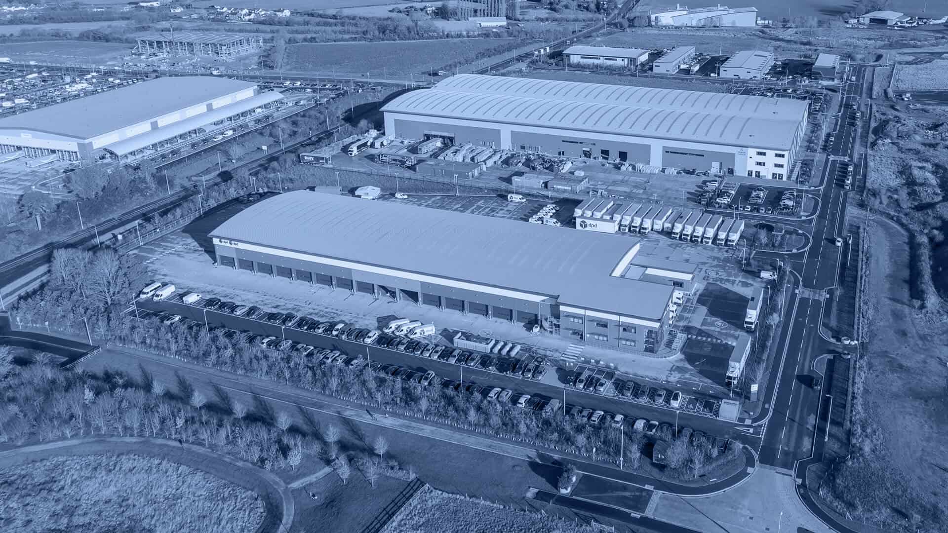 Aerial view of an industrial complex with large warehouses surrounded by roads and fields.